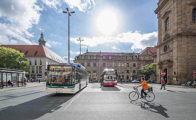 Platz mit Stadtbussen und Fahrrädern umringt von historischen Gebäuden